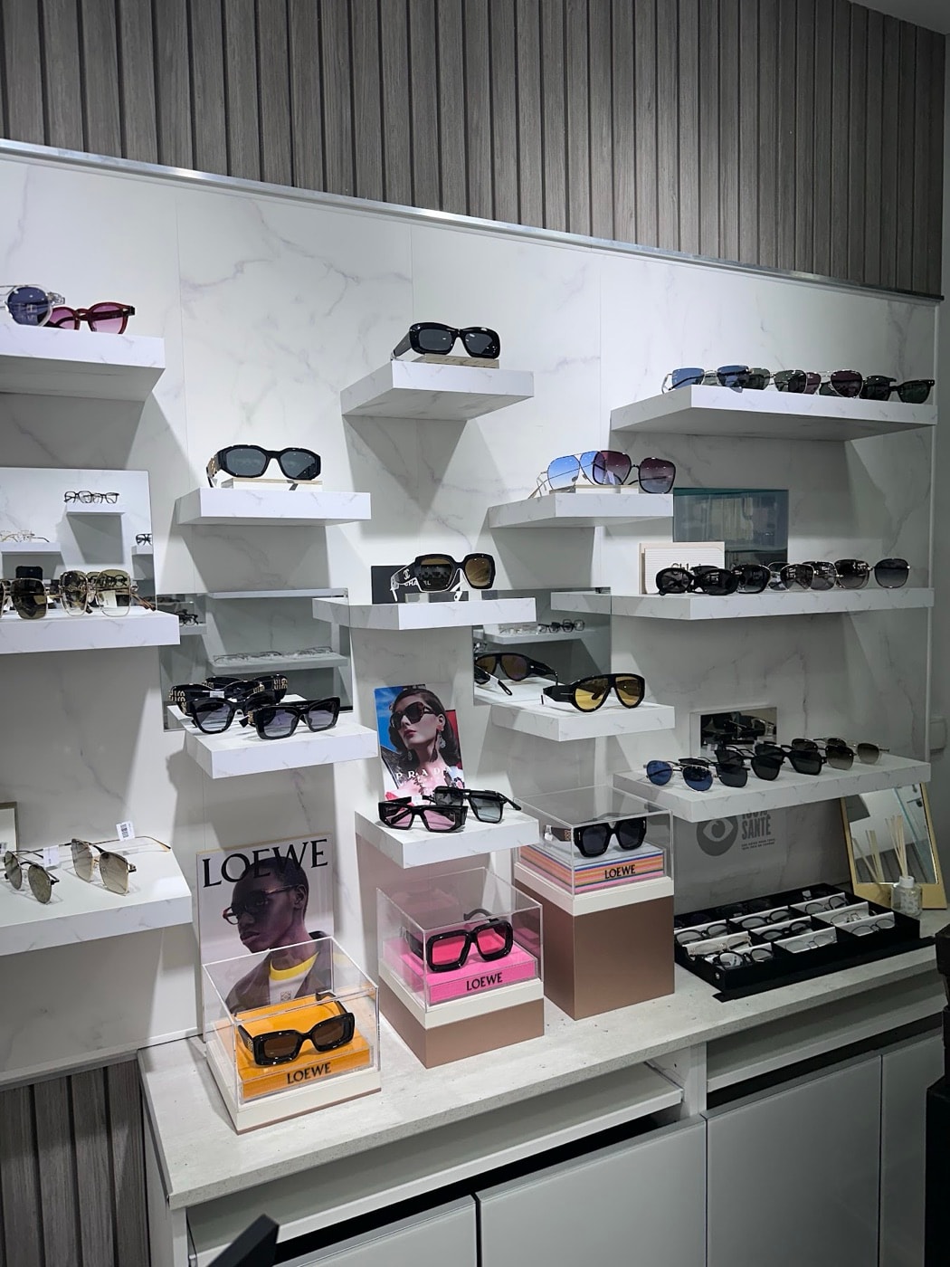 Le mur de solaires de la boutique : étagères de marbre blanc, montures Loewe, Prada, Chanel et Miu Miu